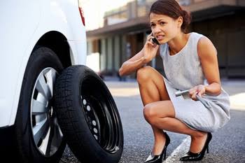 Driver waiting beside a car with a replacement tire leaning against the vehicle