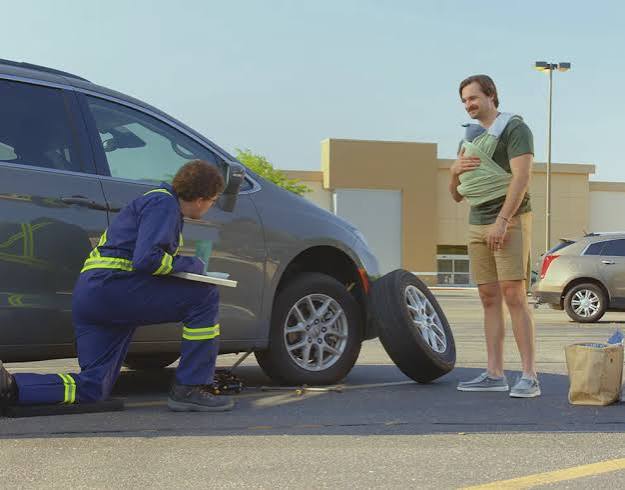 Roadside technician changing a tire while a father and baby wait safely nearby